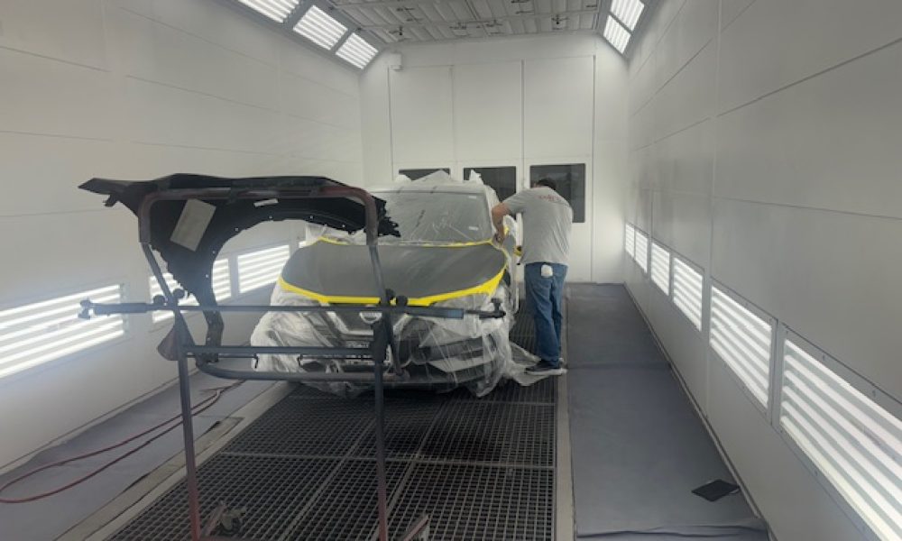 Vehicle prepared for refinishing inside the Core Collision Georgetown paint booth with a technician masking and prepping the car for paint.
