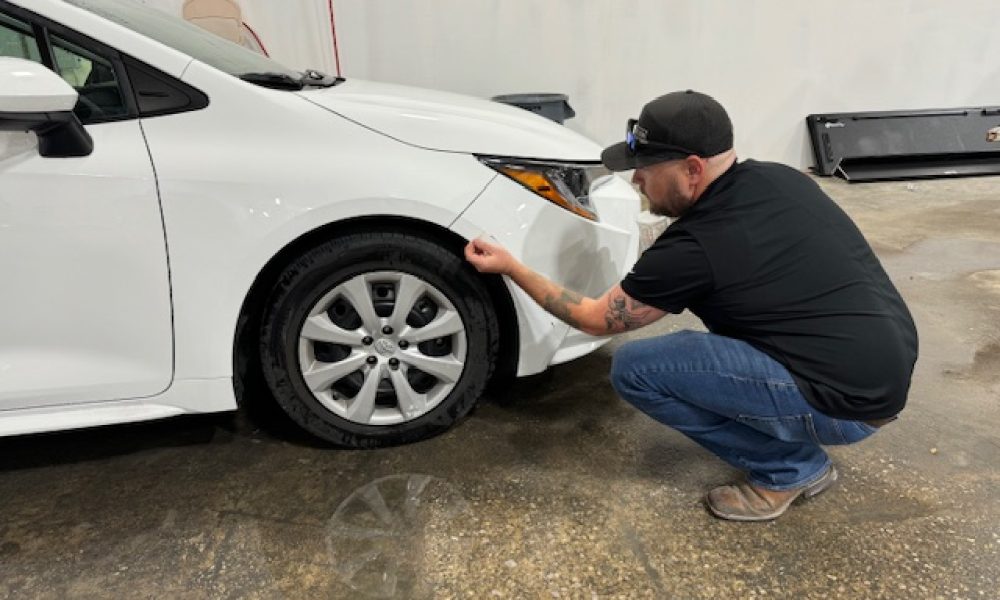 Collision repair technician at Core Collision Georgetown inspecting the front bumper alignment on a white vehicle after body and paint work.