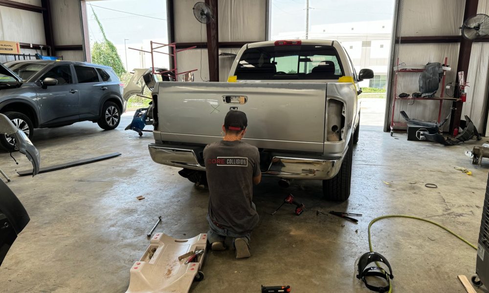 Core Collision technician repairing the rear end of a pickup truck inside the Kyle Buda auto body shop, performing bumper and structural collision repair.