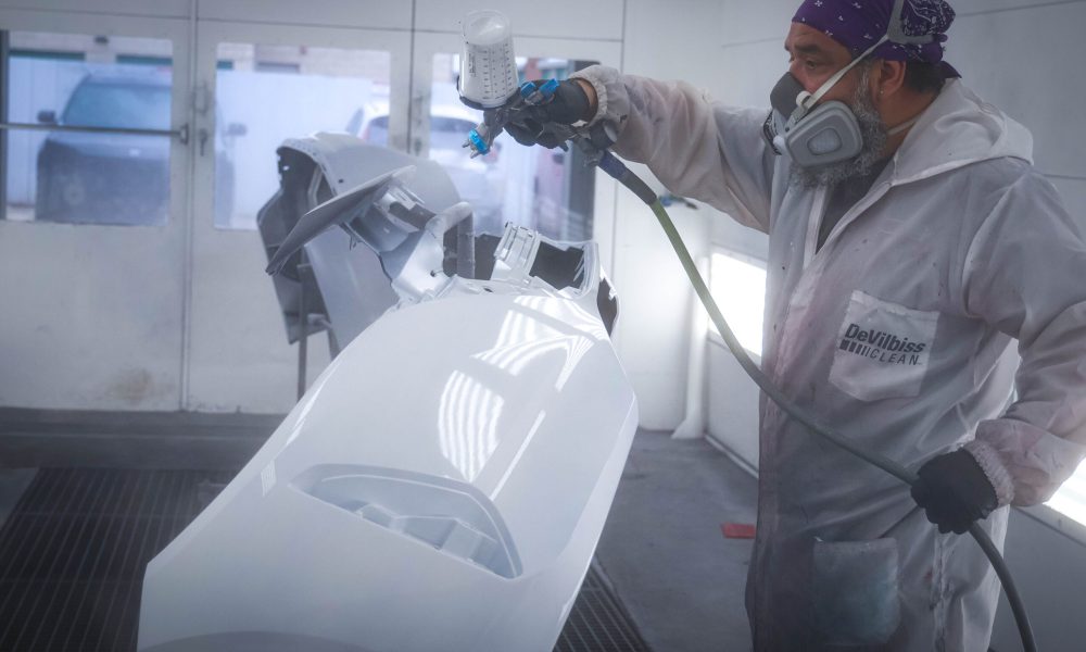 A Core Collision technician applies fresh paint to a vehicle body panel inside a professional paint booth at the Kyle, TX collision repair shop.